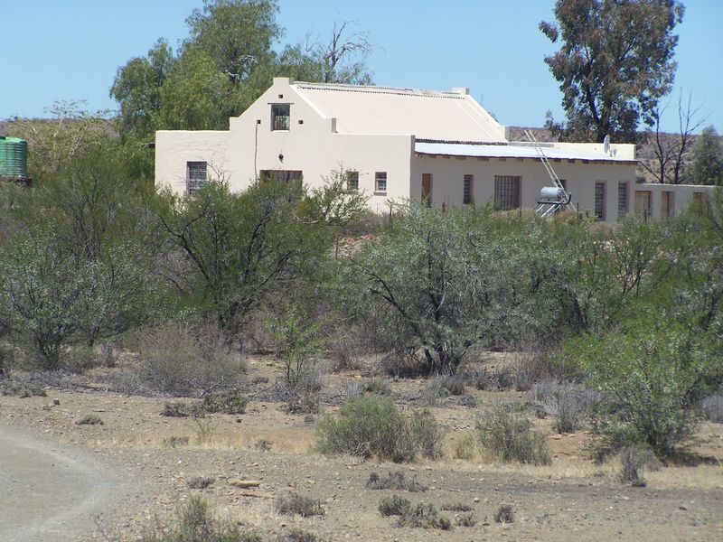 A traditional farm-style dwelling featuring a gabled roof, set within a rural landscape with natural vegetation and a gravel access path.