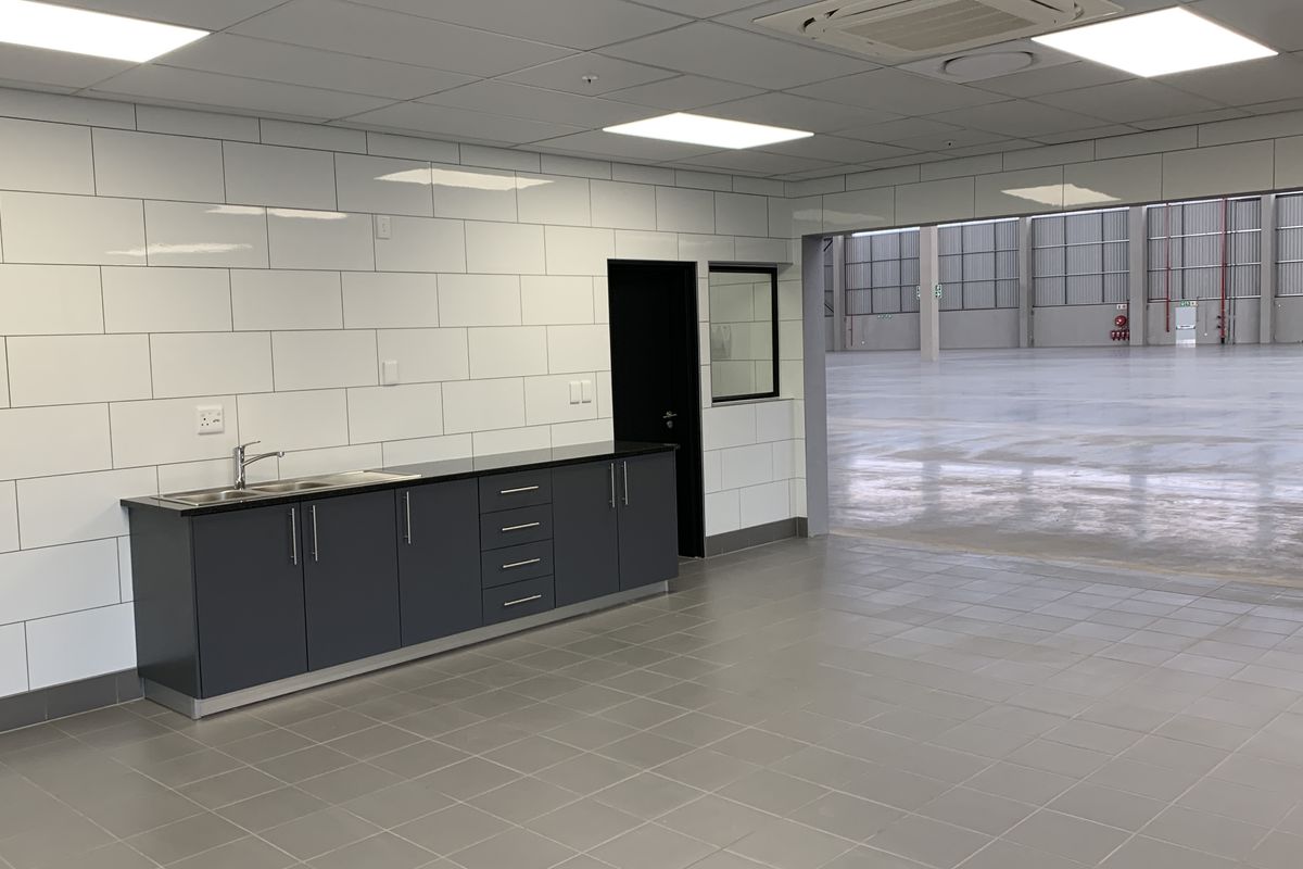 Modern industrial kitchenette featuring dark cabinetry, stainless steel sink, and tiled splashback, with direct access to a large warehouse space.