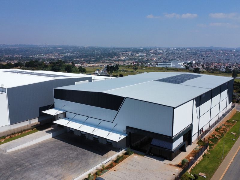 Aerial view of a modern industrial warehouse facility featuring large loading docks, solar panel installations, and a paved yard area.