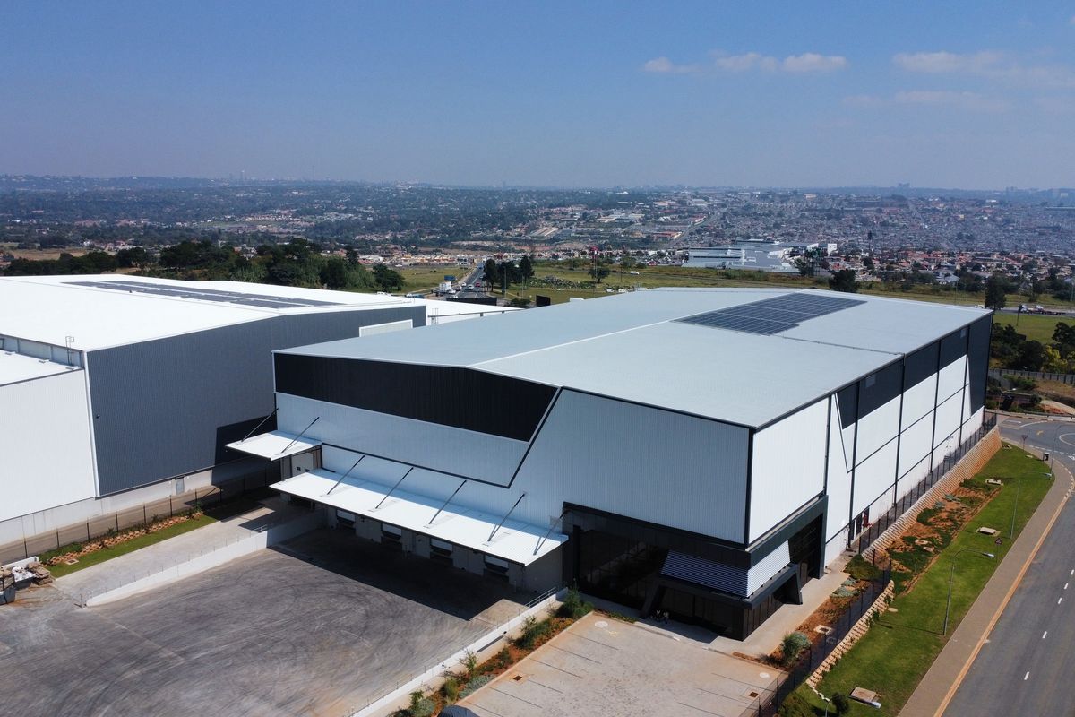 Aerial view of a modern industrial warehouse facility featuring large loading docks, solar panel installations, and a paved yard area.