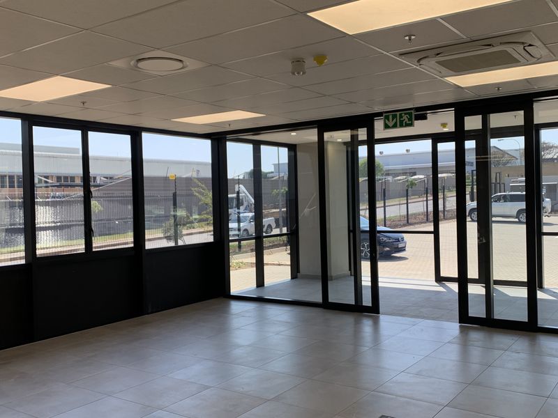 Modern, bright entrance area featuring large aluminium-framed glass doors, tiled flooring, and a suspended ceiling with integrated lighting and air conditioning.