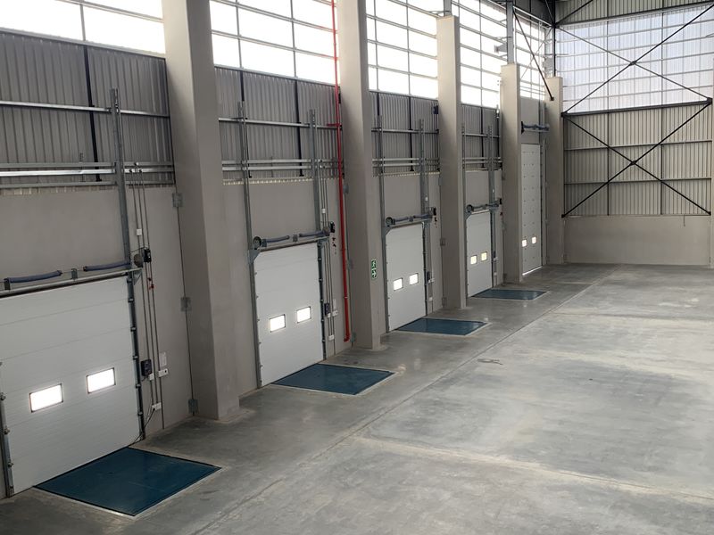 Spacious industrial warehouse interior featuring multiple roller shutter loading doors, high ceilings with natural light panels, and durable concrete flooring.