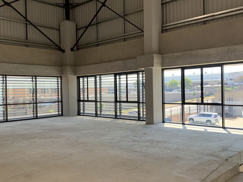 Spacious open-plan industrial area featuring high ceilings with exposed steel trusses, concrete flooring, and extensive aluminium windows providing ample natural light.
