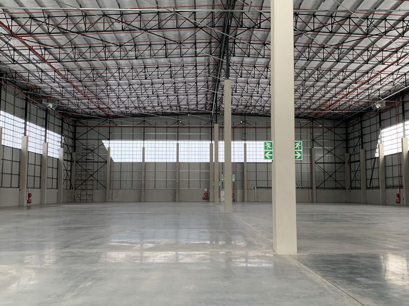 Spacious industrial warehouse featuring high ceilings with exposed steel trusses, polished concrete flooring, and ample natural light through translucent wall panels.