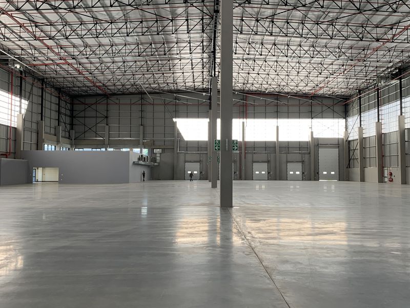 Expansive industrial warehouse space featuring high ceilings, polished concrete flooring, multiple roller shutter doors, and integrated fire sprinkler systems.