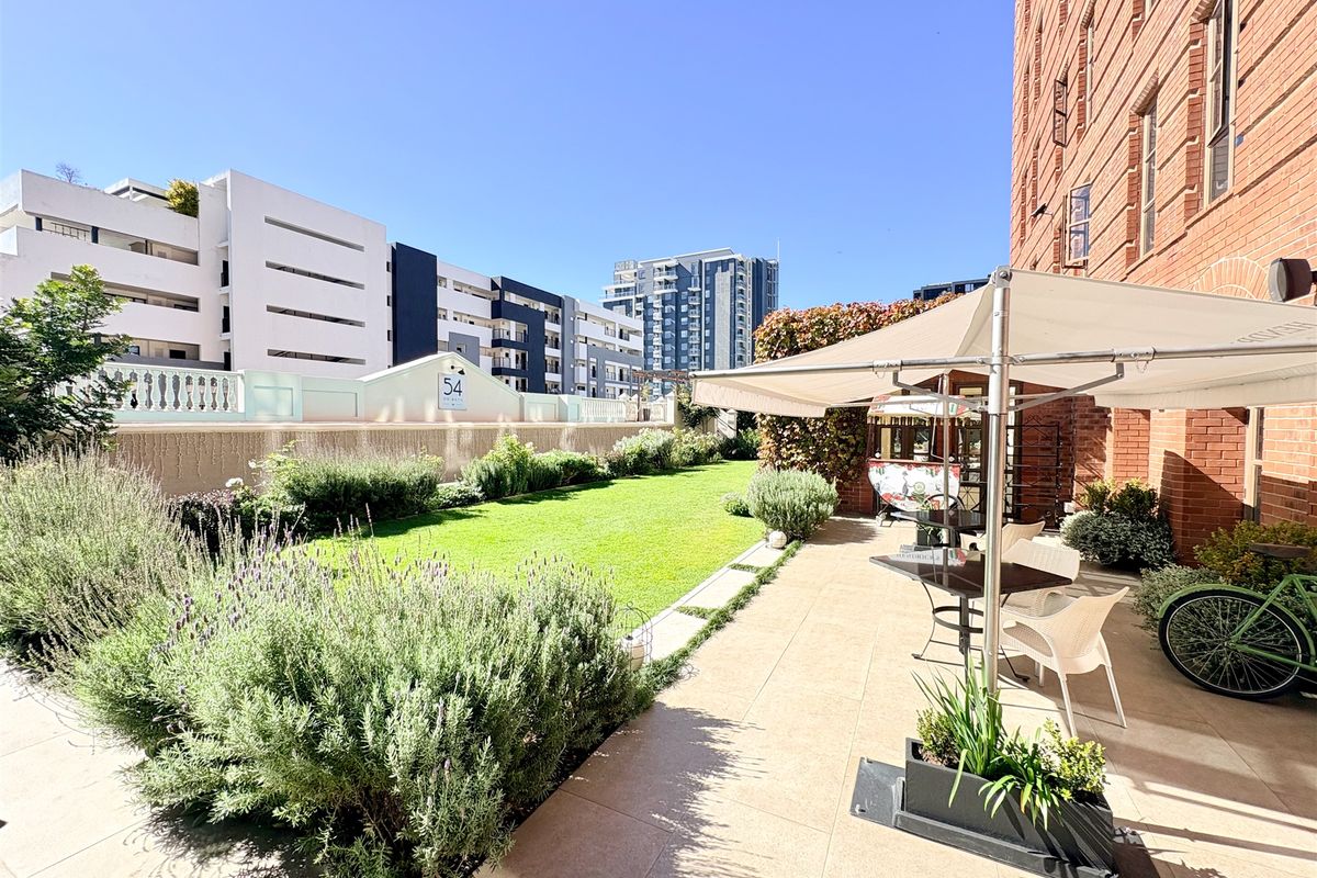 A well-maintained rear patio area featuring tiled flooring, brick building exterior, and a landscaped garden space.