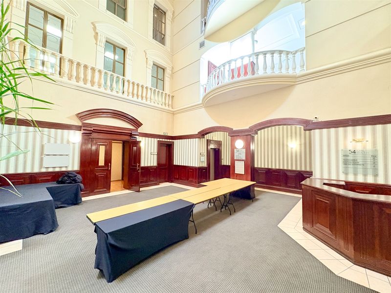 Spacious office building lobby featuring a multi-level atrium, classic wood paneling, reception desk, and elegant balustrade detailing.