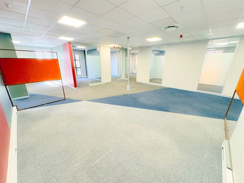 Spacious open-plan office area featuring modern glass partitions, suspended ceilings with recessed lighting, and durable carpet tile flooring.