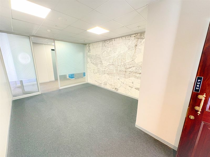 A bright, modern office space featuring glass partitions, a decorative map feature wall, suspended ceiling with recessed lighting, and clean carpet flooring.