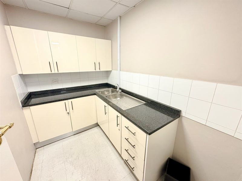 A compact office kitchenette featuring cream-colored cabinetry, dark granite countertops, a stainless steel sink, and a tiled backsplash.