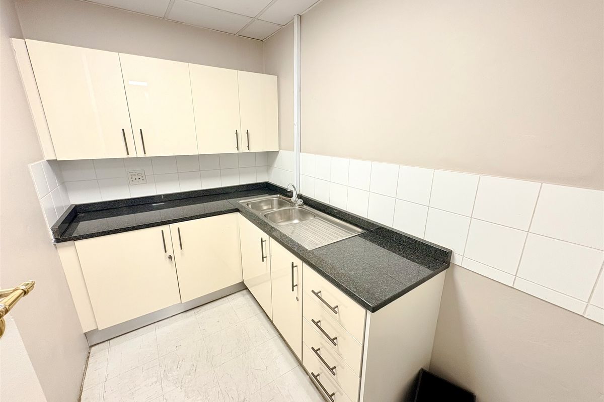 A compact office kitchenette featuring cream-colored cabinetry, dark granite countertops, a stainless steel sink, and a tiled backsplash.