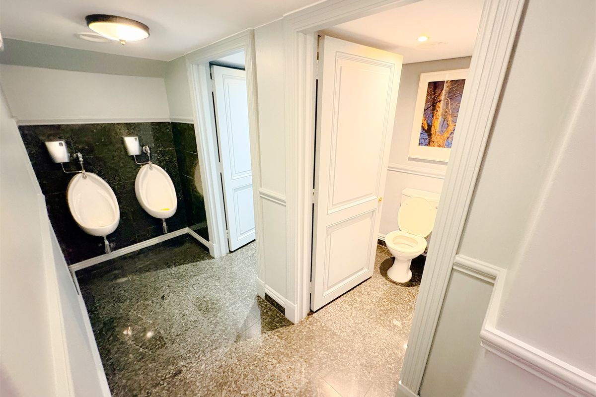 A clean, well-maintained office restroom featuring granite flooring and wall cladding, equipped with two urinals and a private toilet cubicle.