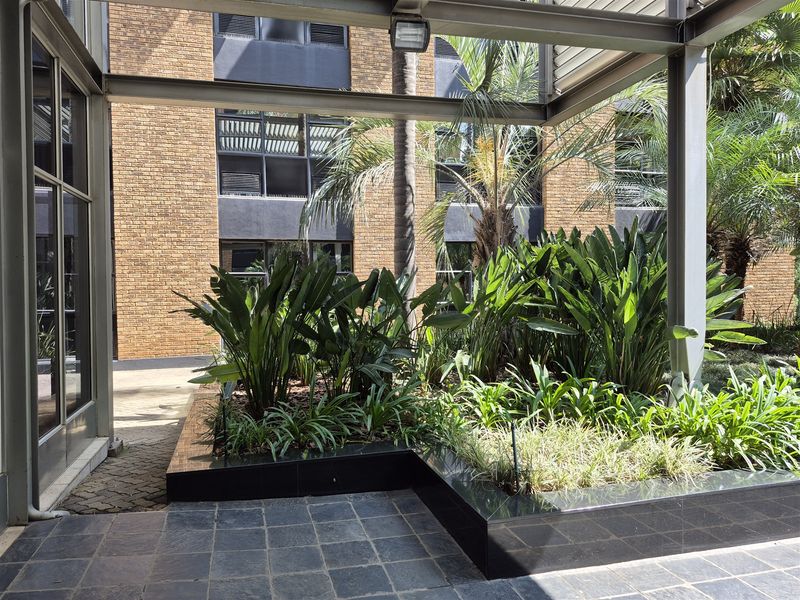 A well-maintained covered patio area featuring a steel pergola structure, stone flooring, and a modern raised granite planter box set against a brick building facade.