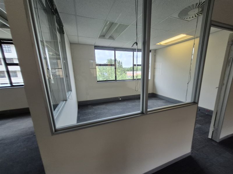 An empty office space featuring glass partitions, carpet tiles, and a suspended ceiling with recessed lighting, offering a functional workspace environment.