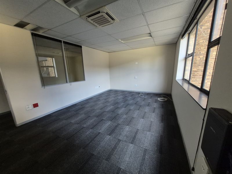 A vacant office space featuring carpet tiles, a suspended ceiling with integrated air conditioning, and large windows providing natural light.