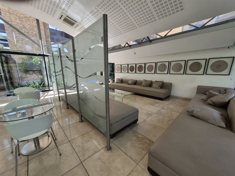 Modern office reception or lounge area featuring tiled flooring, glass partitions, and floor-to-ceiling windows providing ample natural light.