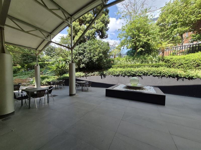 A well-maintained covered outdoor patio area featuring stone tiling, a modern water feature, and a landscaped garden backdrop.