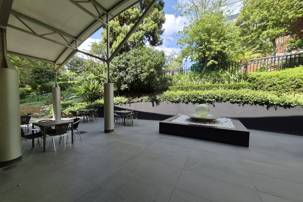A well-maintained covered outdoor patio area featuring stone tiling, a modern water feature, and a landscaped garden backdrop.