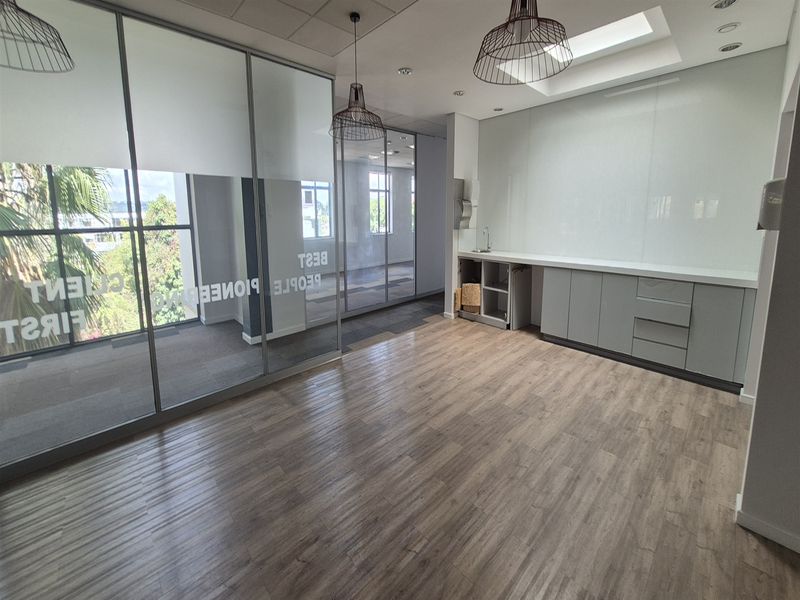 Modern office space featuring glass partitions, wood-look laminate flooring, a built-in kitchenette area, and a skylight providing natural light.