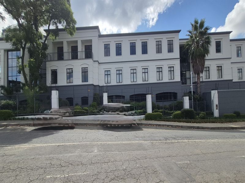 A professional multi-story office building facade featuring a modern exterior, secure perimeter fencing, and a paved entrance area.