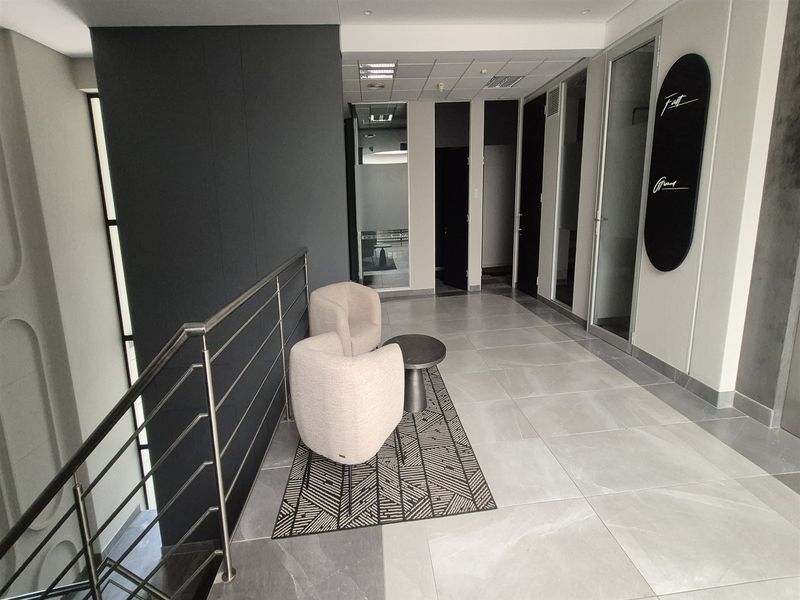 Modern office hallway featuring large format floor tiles, stainless steel balustrades, and glass-paneled office doors with recessed ceiling lighting.