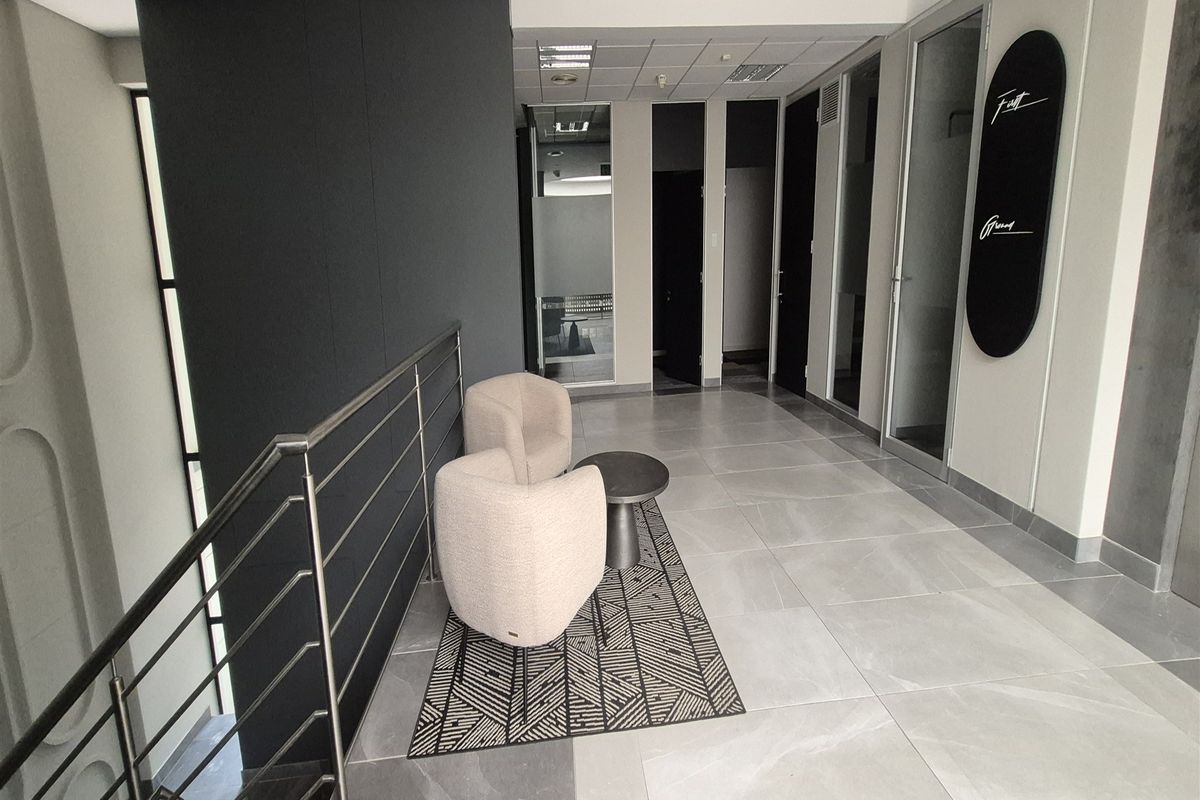 Modern office hallway featuring large format floor tiles, stainless steel balustrades, and glass-paneled office doors with recessed ceiling lighting.