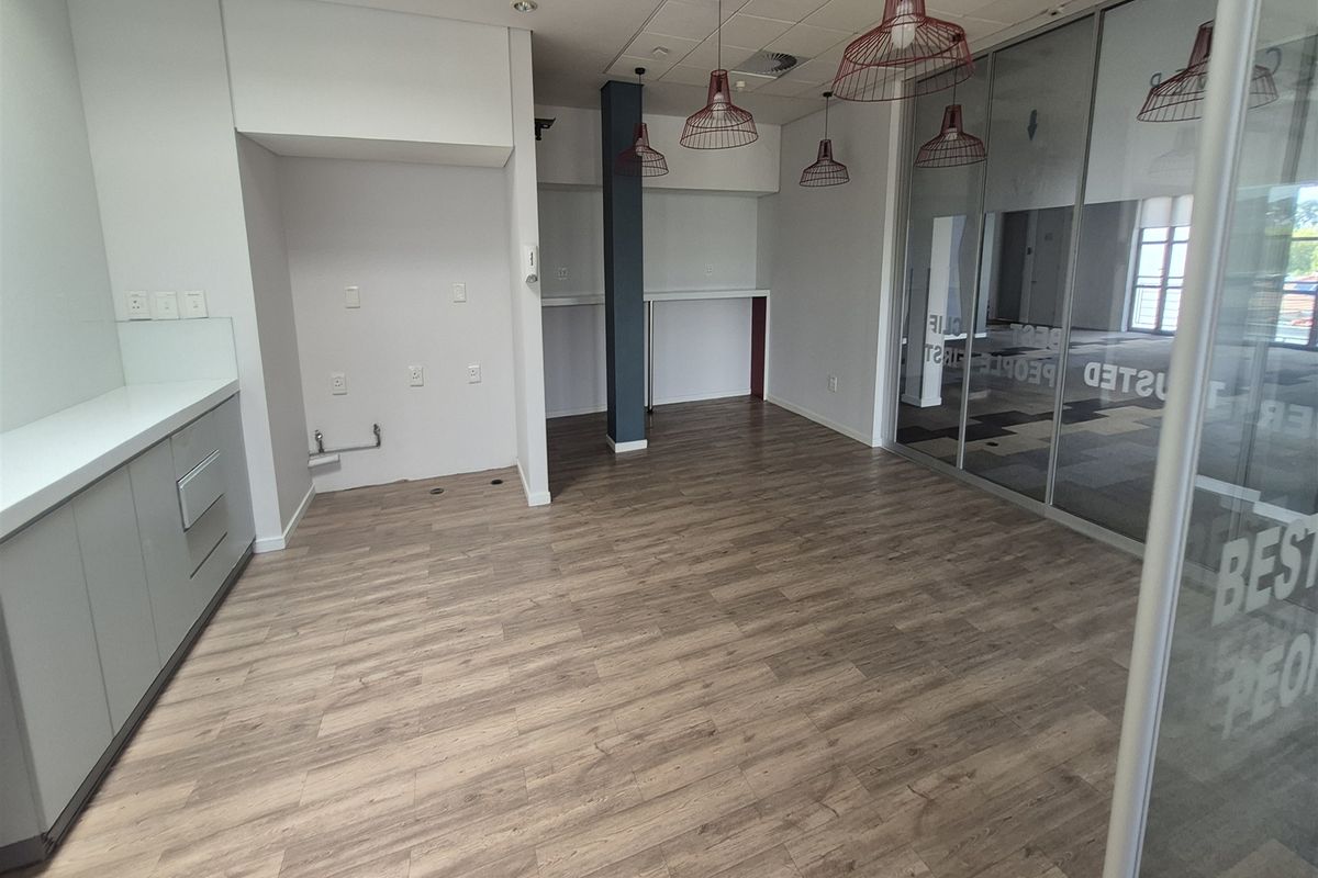 A modern, empty office kitchenette featuring sleek cabinetry, wood-look laminate flooring, and a glass partition wall, providing a clean and professional workspace environment.