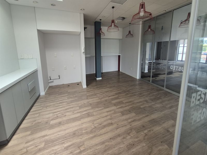 A modern, empty office kitchenette featuring sleek cabinetry, wood-look laminate flooring, and a glass partition wall, providing a clean and professional workspace environment.