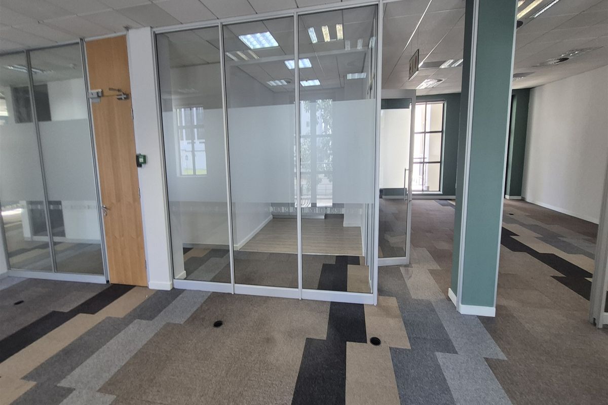 Modern open-plan office space featuring glass partition walls, suspended ceilings, and contemporary patterned carpet tiles, offering a bright and professional work environment.