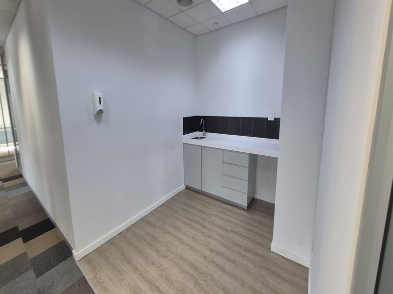 A clean, functional utility kitchenette area featuring built-in cabinetry, a sink, and modern laminate flooring within an office environment.