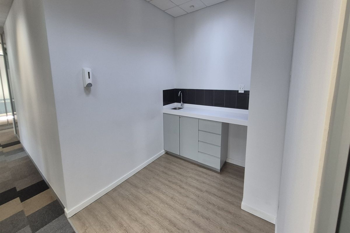 A clean, functional utility kitchenette area featuring built-in cabinetry, a sink, and modern laminate flooring within an office environment.