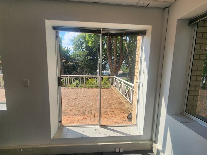 Empty office space featuring a sliding glass door that opens onto a private brick-paved balcony with metal railings.