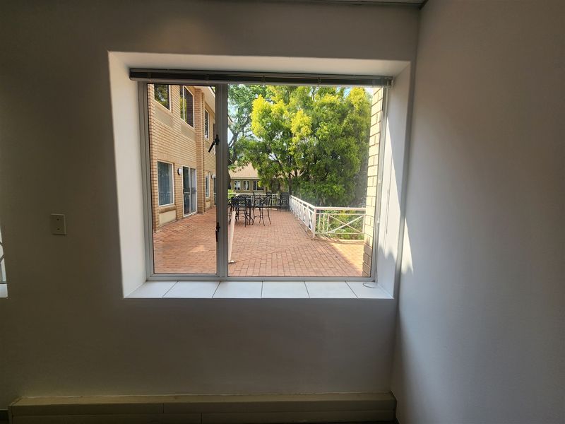 A bright, empty office space featuring a large window with a view overlooking an outdoor brick-paved patio area.