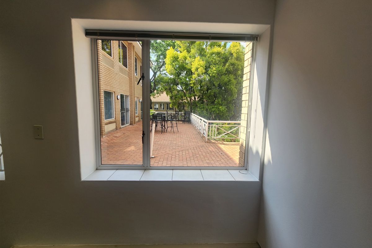 A bright, empty office space featuring a large window with a view overlooking an outdoor brick-paved patio area.