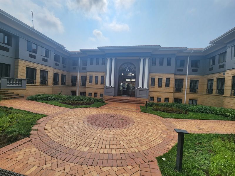 A well-maintained office building courtyard featuring a circular paved design, landscaped garden beds, and a prominent entrance with classical columns.
