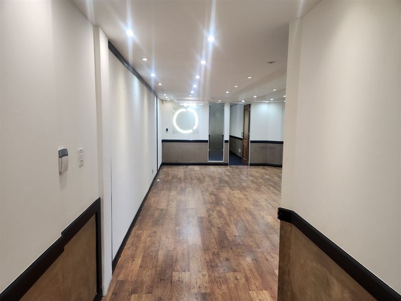 A spacious, empty office area featuring wood-look laminate flooring, recessed downlighting, and decorative wainscoting, providing a clean and professional workspace environment.