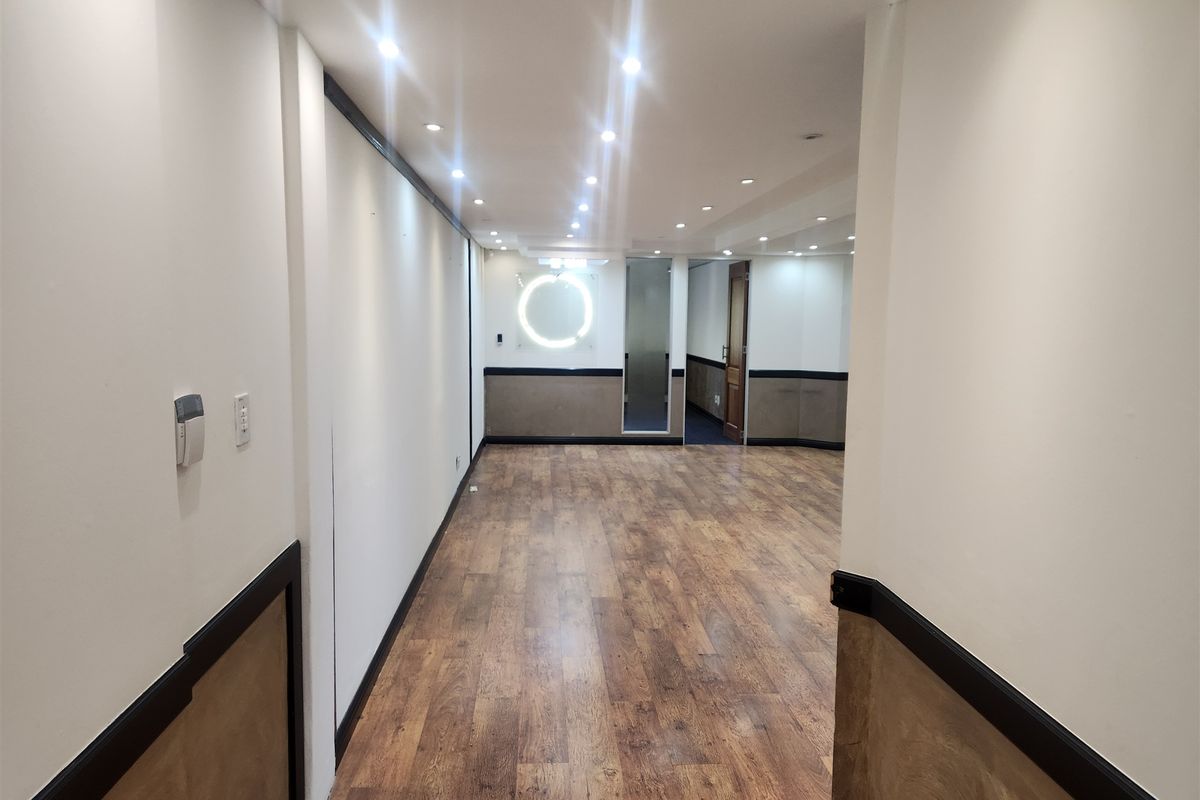 A spacious, empty office area featuring wood-look laminate flooring, recessed downlighting, and decorative wainscoting, providing a clean and professional workspace environment.