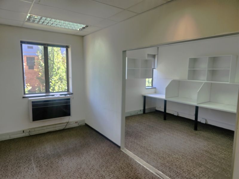 An empty office space featuring built-in desks, integrated shelving, carpeted flooring, and a window-mounted air conditioning unit.