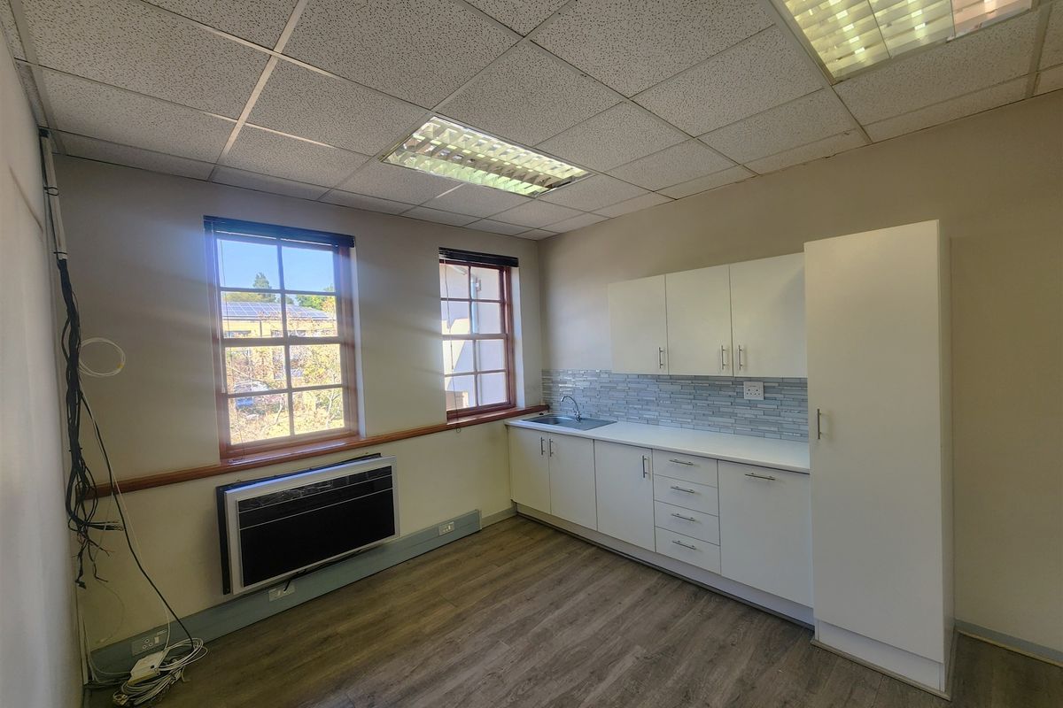 A functional office kitchenette featuring white cabinetry, a stainless steel sink, tiled backsplash, and wood-look laminate flooring.