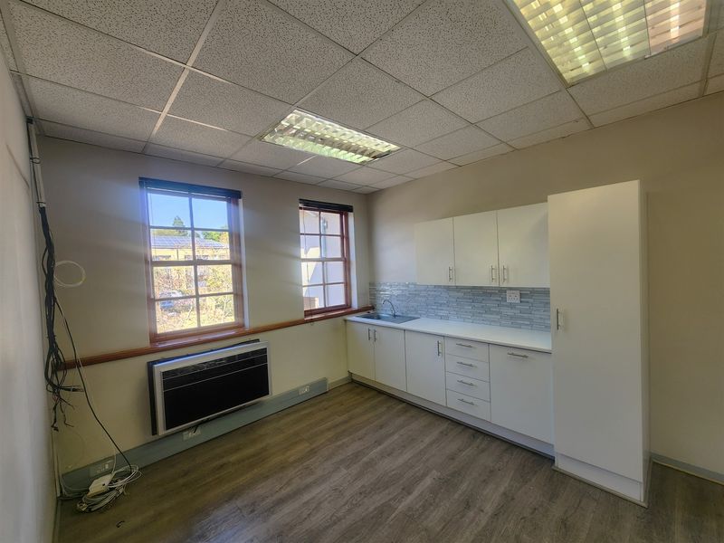 A functional office kitchenette featuring white cabinetry, a stainless steel sink, tiled backsplash, and wood-look laminate flooring.