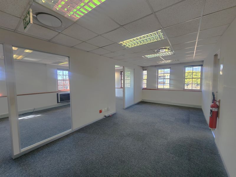 A vacant, open-plan office space featuring a suspended ceiling, recessed lighting, carpeted flooring, and a glass partition, offering a functional professional environment.
