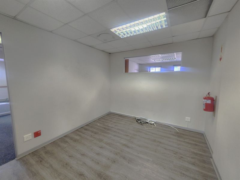 A clean, empty office space featuring laminate flooring, a suspended ceiling with recessed lighting, and an internal window for added natural light.