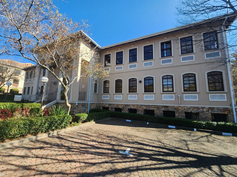 A well-maintained office building exterior featuring stone cladding, arched windows, and a paved parking area with mature landscaping.