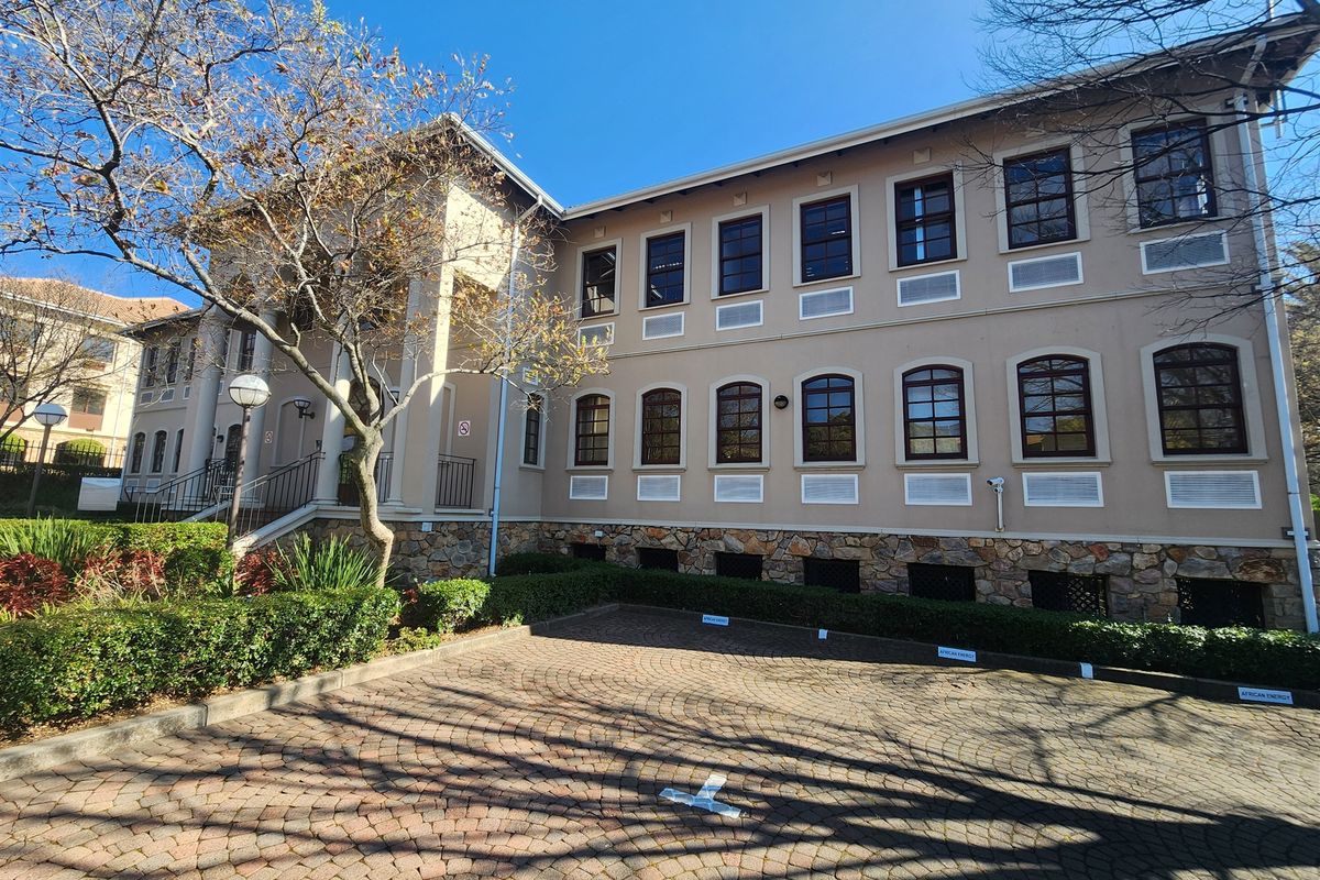 A well-maintained office building exterior featuring stone cladding, arched windows, and a paved parking area with mature landscaping.