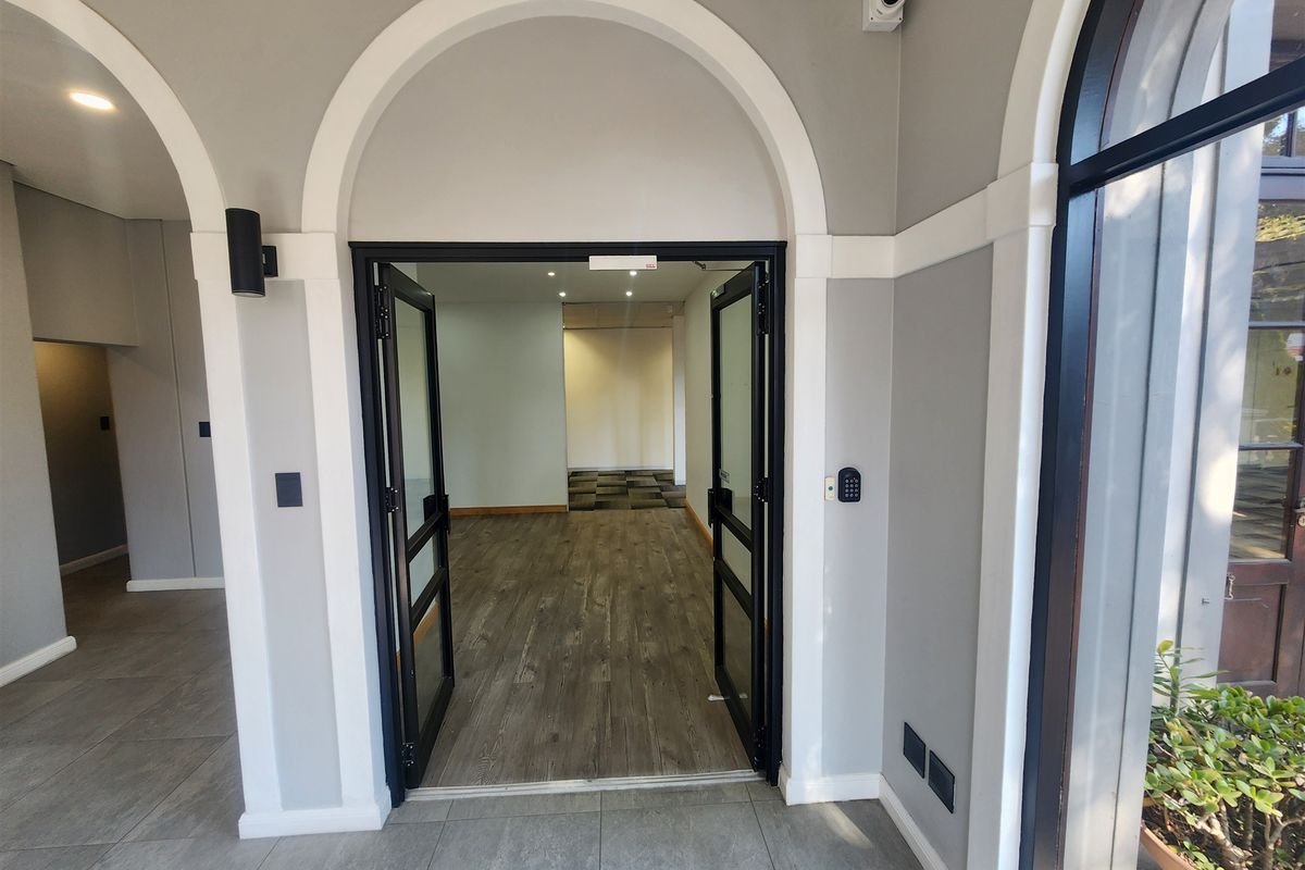A clean, modern office entrance featuring arched architectural detailing, secure keypad access, recessed lighting, and a combination of tiled and laminate flooring.