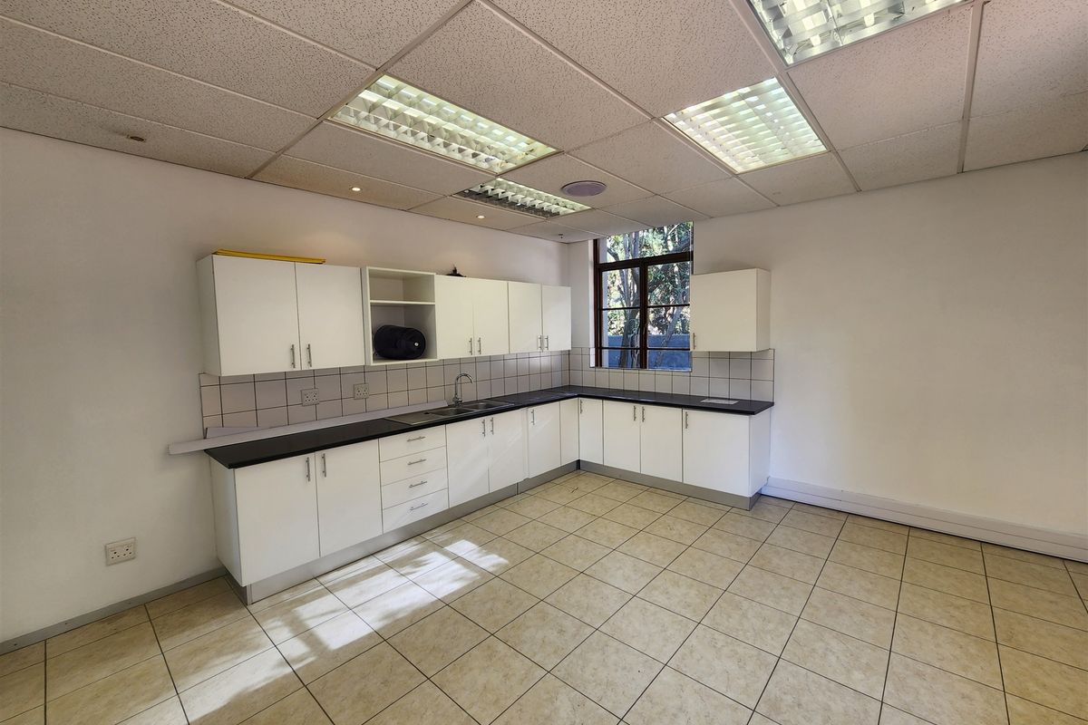 A functional office kitchenette featuring white cabinetry, dark laminate countertops, a stainless steel sink, and tiled flooring under a drop ceiling.