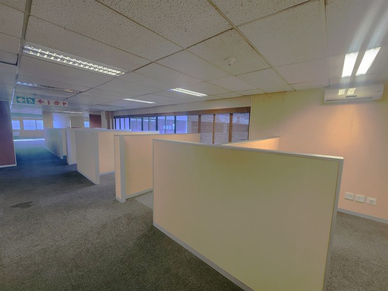 Open-plan office space featuring modular partition walls, suspended ceilings with recessed lighting, and wall-mounted air conditioning units.