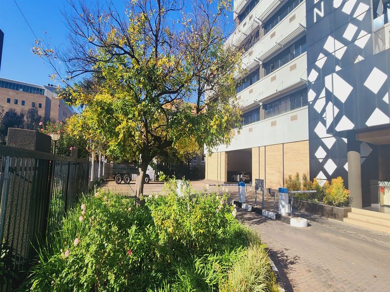 Front exterior view of the office building featuring a paved driveway, security access control, and well-maintained landscaped garden area.