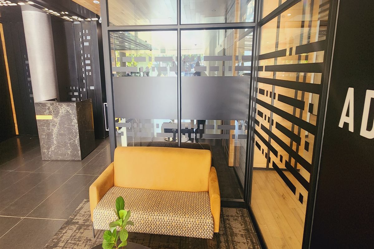 Modern office reception area featuring a sleek marble-look desk, glass partition walls with privacy film, and contemporary tiled flooring.