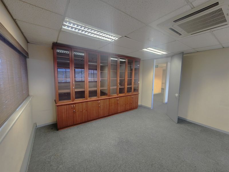 A clean, vacant office space featuring built-in wooden storage cabinetry, carpeted flooring, and integrated ceiling-mounted air conditioning.